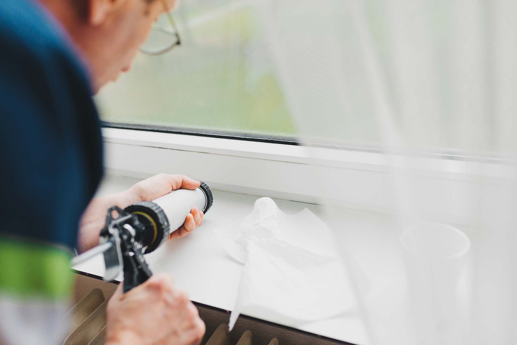 Energy Savings Tips for Summer Blog Image of a man caulking a windowsill